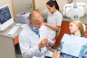 dentist in exam room with patient using a model to explain procedure