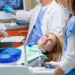 woman in dental exam room with hygienist and dentist